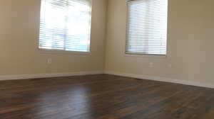 Unfurnished room with baseboards, dark wood finished floors, and visible vents