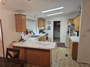 Kitchen with electric range, independent washer and dryer, light wood-type flooring, light countertops, and freestanding refrigerator