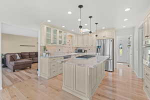 Kitchen with cream cabinets, light stone countertops, light wood-style flooring, stainless steel appliances, and tasteful backsplash