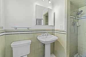 Bathroom with toilet, tile walls, a tile shower, and a wainscoted wall