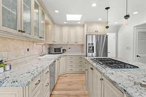 Kitchen with a skylight, cream cabinets, a sink, light wood-style floors, and stainless steel appliances