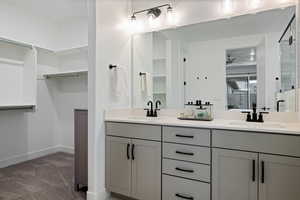 Ensuite bathroom with double vanity, baseboards, ceiling fan, and a sink