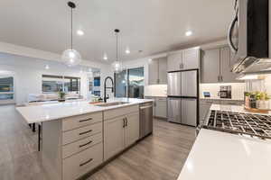 Kitchen with gray cabinets, appliances with stainless steel finishes, a sink, light countertops, and light wood finished floors