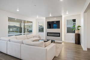Living room with a glass covered fireplace, baseboards, recessed lighting, and wood finished floors