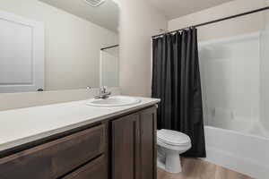 Full bathroom with vanity, wood finished floors, toilet, and shower / bath combo with shower curtain