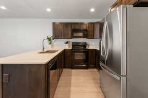 Kitchen with dark brown cabinetry, light wood-type flooring, a sink, light countertops, and black appliances