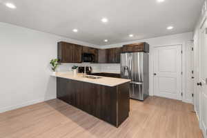Kitchen featuring dark brown cabinets, black microwave, light countertops, a peninsula