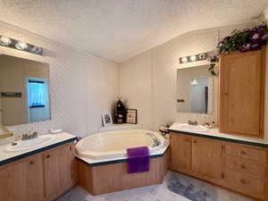 Primary Bathroom featuring a sink, a bath, vaulted ceiling, and a textured ceiling