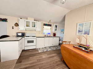 Kitchen with white gas range oven, black microwave, a peninsula, white cabinetry, and dark flooring