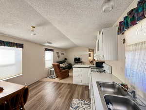 Kitchen with white gas range oven, a sink, a textured ceiling, under cabinet range hood, and dark floors