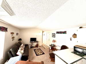 Living area with carpet floors, a textured ceiling, and vaulted ceiling