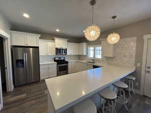 Kitchen with backsplash, dark wood-style flooring, a sink, a peninsula, and stainless steel appliances