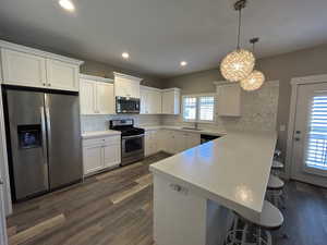 Kitchen featuring decorative backsplash, a peninsula, a kitchen bar, a sink, and appliances with stainless steel finishes