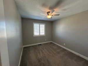 Empty room with ceiling fan, a textured ceiling, visible vents, baseboards, and dark carpet