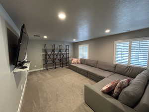 Carpeted living area with visible vents, recessed lighting, baseboards, and a textured ceiling