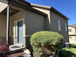 View of side of property featuring stucco siding, cooling unit, and stone siding