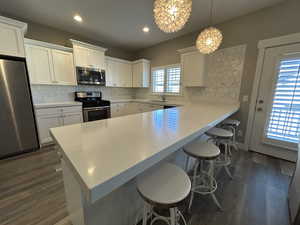 Kitchen featuring decorative backsplash, dark wood-style flooring, a kitchen breakfast bar, a sink, and stainless steel appliances