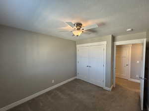 Unfurnished bedroom featuring baseboards, a ceiling fan, a closet, and dark colored carpet