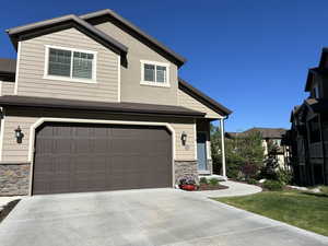 View of front of house featuring an attached garage, driveway, a shingled roof, and stone siding