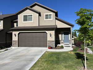 View of front facade featuring a garage, a front lawn, driveway, and stone siding