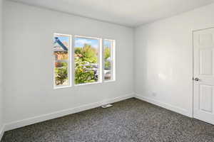 Empty room with dark colored carpet, baseboards, and visible vents