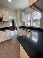 Kitchen with a sink, a healthy amount of sunlight, white cabinetry, dark wood-type flooring, and white microwave