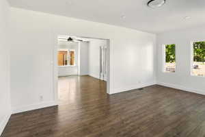 Unfurnished room featuring baseboards, dark wood-style flooring, and ceiling fan