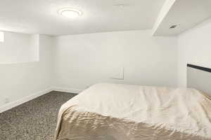 Bedroom with a textured ceiling, baseboards, visible vents, and dark carpet