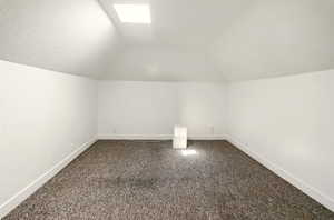 Additional living space featuring baseboards, vaulted ceiling, and dark carpet