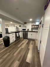 Kitchen with a sink, dark wood-style flooring, white cabinetry, dark countertops, and appliances with stainless steel finishes