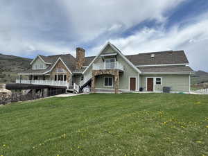 Back of house featuring cooling unit, a balcony, a lawn, and a chimney