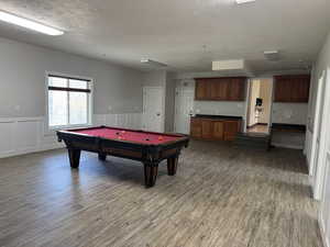 Recreation room featuring light wood-style floors, billiards table, a wainscoted wall, a textured ceiling, and a decorative wall