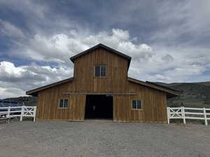View of barn with gravel driveway, fence, and a mountain view