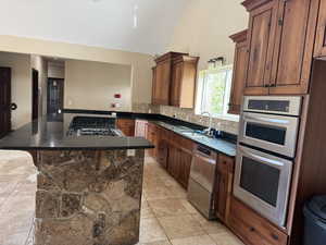 Kitchen featuring a sink, stainless steel appliances, dark countertops, a towering ceiling, and tasteful backsplash