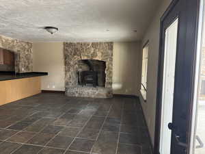 Unfurnished living room featuring a wood stove, baseboards, a textured ceiling, and plenty of natural light