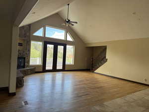 Unfurnished living room featuring ceiling fan, high vaulted ceiling, stairs, a premium fireplace, and wood finished floors