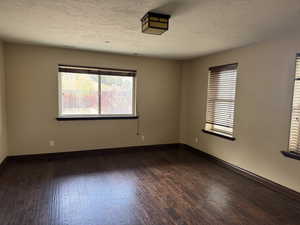 Spare room with dark wood-style flooring, healthy amount of natural light, a textured ceiling, and baseboards