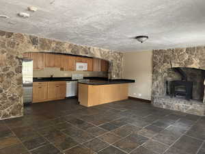 Kitchen featuring white appliances, dark countertops, a wood stove, baseboards, and a peninsula