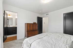 Bedroom with visible vents, connected bathroom, baseboards, and light colored carpet