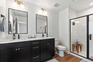 Full bath with a sink, a stall shower, toilet, and wood finished floors