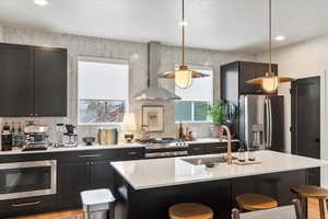 Kitchen featuring wall chimney range hood, a kitchen bar, light countertops, a sink, and stainless steel appliances