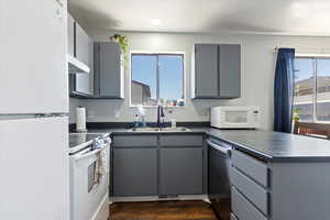 Kitchen with gray cabinetry, a sink, dark countertops, and white appliances