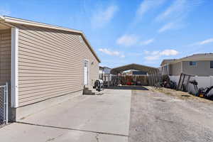 View of property exterior featuring concrete driveway, entry steps, fence, and a detached carport