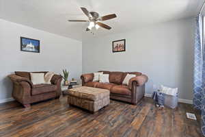 Living area with a ceiling fan, baseboards, visible vents, and dark wood-style floors