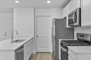 Kitchen with a peninsula, white cabinets, a sink, light wood-style flooring, and stainless steel appliances