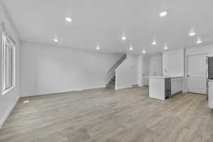 Unfurnished living room with visible vents, a sink, baseboards, stairway, and recessed lighting