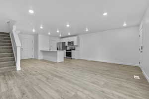 Unfurnished living room with stairway, baseboards, light wood finished floors, and recessed lighting