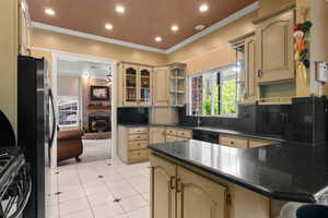 Kitchen featuring freestanding refrigerator, ornamental molding, a peninsula, dark countertops, and cream cabinets