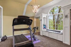 Workout room with visible vents, dark carpet, lofted ceiling, and a notable chandelier