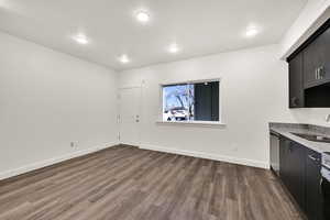 Kitchen with dark cabinets, light stone counters, dark wood-type flooring, dishwasher, and recessed lighting